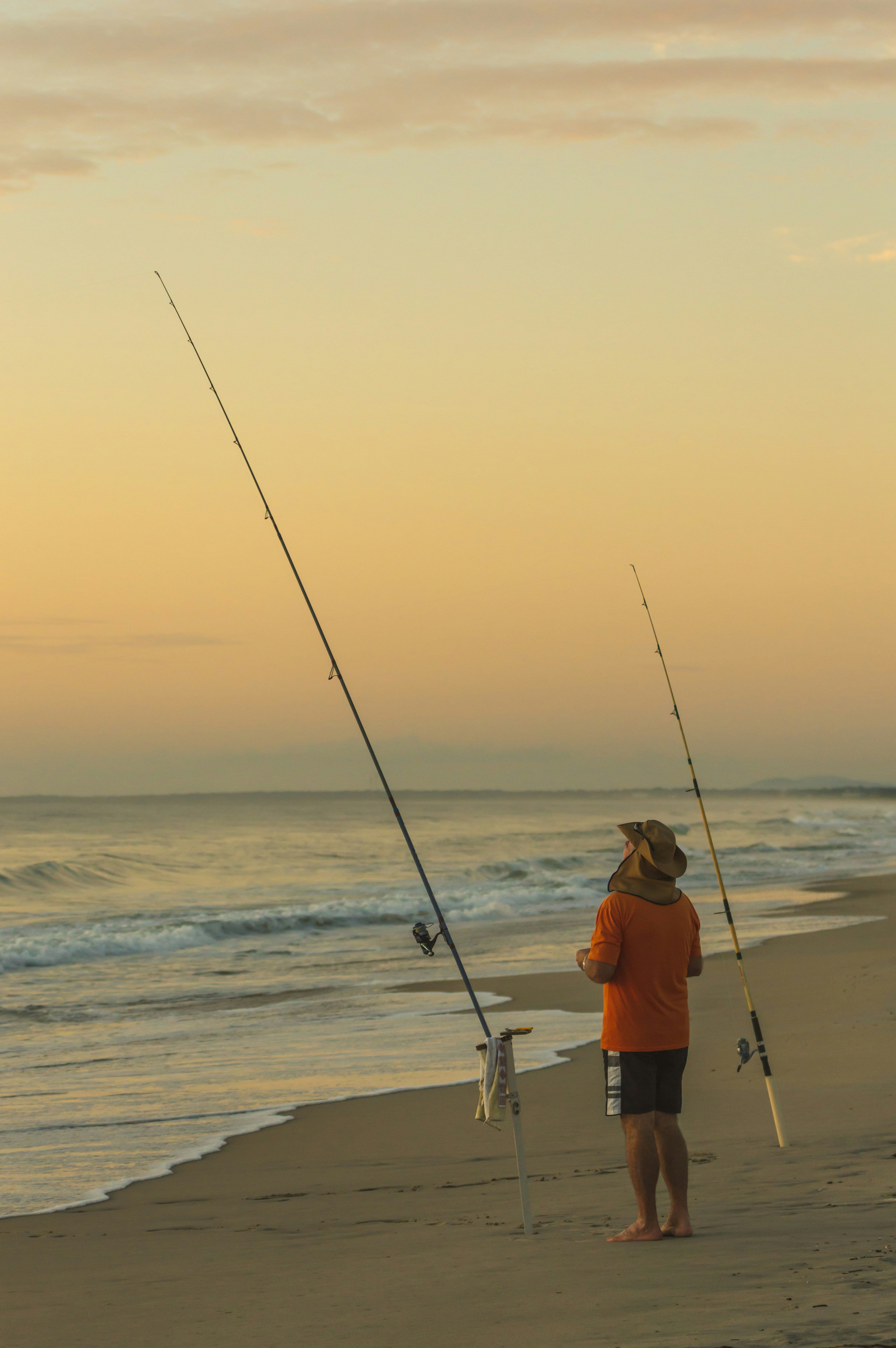 man in orange shirt fishing on sea during daytime